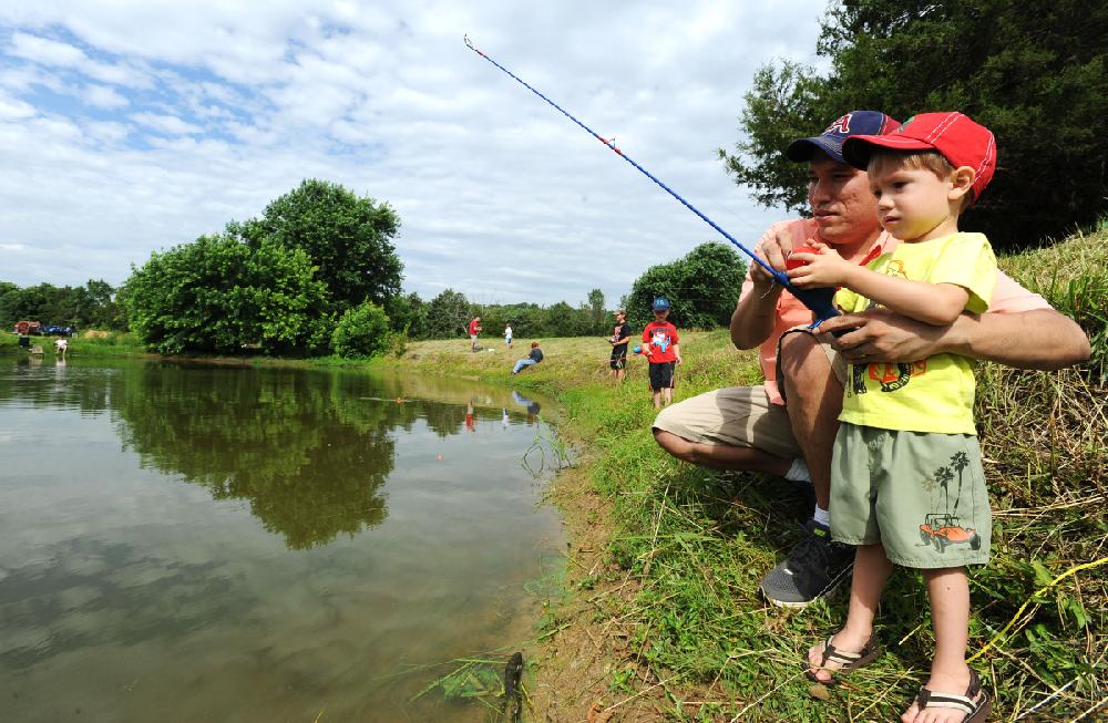 NWA Media/ANDY SHUPE - Devon Wilson of Fayetteville helps his 2-year-old son Gabriel Wilson to cast his line during a fishing derby organized by the Elkins Public Library Thursday, June 19, 2014, at the Carter Pond in Elkins. Prizes were given for the largest and smallest fish caught.