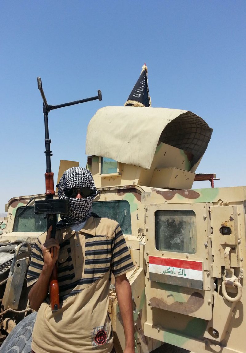 A militant stands with a captured Iraqi army Humvee at a checkpoint Thursday outside the Beiji refinery, about 155 miles north of Baghdad. The fighting at Beiji comes as Iraq has asked the U.S. for airstrikes targeting the militants from the Islamic State of Iraq and the Levant.