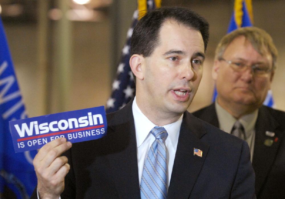 FILE - In this March 17, 2011 file photo Wisconsin Gov. Scott Walker holds a bumper sticker with his signature campaign promise for the state as he announces a new manufacturer will move to Pleasant Prairie, near Kenosha, Wis. Best known for effectively ending collective bargaining in the state and surviving a recall election, the Republican governor's re-election bid is now facing a major campaign issue over something he didn't go. Walker promised in 2010 that over four years the state would add 250,000 private sector jobs: Now three years into his term he's less than halfway there. (AP Photo/Journal Times, Mark Hertzberg, File)