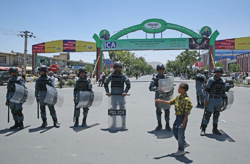 An Afghan boy walks past Afghanistan police forces standing guard Saturday during a protest by supporters of presidential candidate Abdullah Abdullah in Kabul.