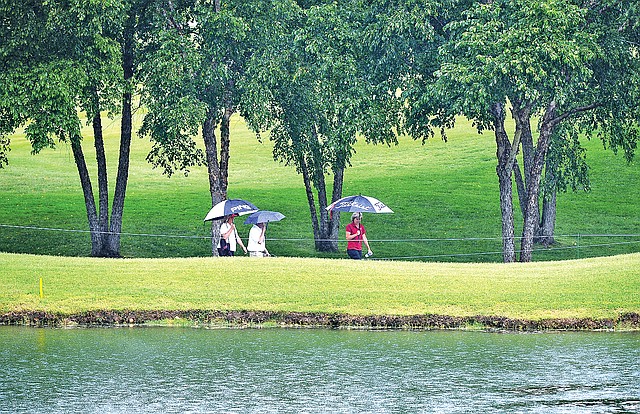 STAFF PHOTO SAMANTHA BAKER &#8226; @NWASAMANTHA Spectators protect themselves from the rain on the way to the 16th green Monday at Pinnacle Country Club in Rogers during the Walmart NW Arkansas Championship local qualifying tournament.
