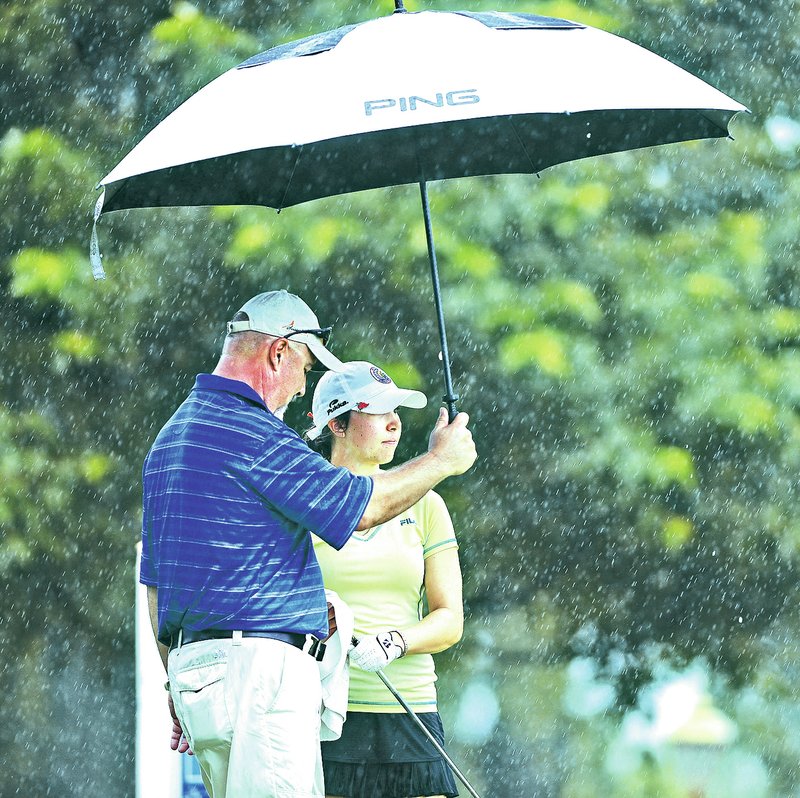 STAFF PHOTO SAMANTHA BAKER &#8226; @NWASAMANTHA A man holds an umbrella over Alex Stewart of Oklahoma City before she tees off on the 15th hole Monday at Pinnacle Country Club in Rogers during the Walmart NW Arkansas Championship local qualifying tournament.