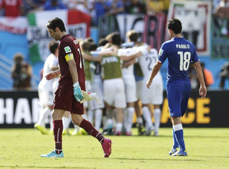 Italy’s goalkeeper Gianluigi Buffon (left) and Marco Parolo walk off the field as Uruguay’s players celebrate a 1-0 victory in Natal, Brazil, that eliminated the Italians from World Cup competition.