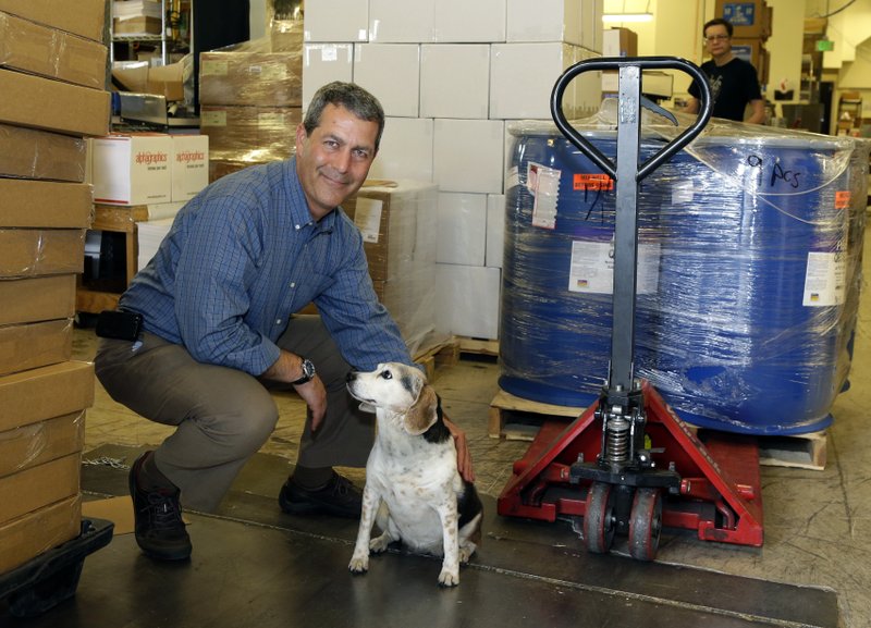 In this Monday, June 23, 2014 photo, Chuck Stempler, owner of an AlphaGraphics printing and marketing franchise, poses for a photo with his dog, Dagny, in the shipping and receiving area of his business, in Seattle. Stempler, who is a plaintiff in a federal lawsuit seeking to overturn a Seattle law that will raise the city's minimum wage to $15 from the current $9.32, says he will have to cut jobs to afford the higher wage.