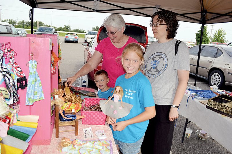 Isabella Desalvo, 8, holds a Barbie that is wearing an outfit made by Marsha Phillips, back left. Shopping in Phillips’ booth at the Conway Farmers Market is Jalisha Vandiver, right. Also pictured is Dylan Strack, 3, who attends the farmers market with relatives who have a produce booth, and he sometimes helps Phillips make hangers for doll clothes. Phillips gives all her proceeds to Soaring Wings Ranch in Holland in Faulkner County.