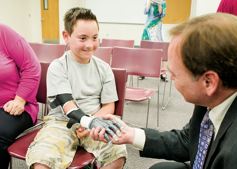 Stephen Schoonmaker, right, College of the Ouachitas president, shakes the newly fitted Robohand of Chicago resident Ryan, 8, who was born with no right arm from the elbow down.