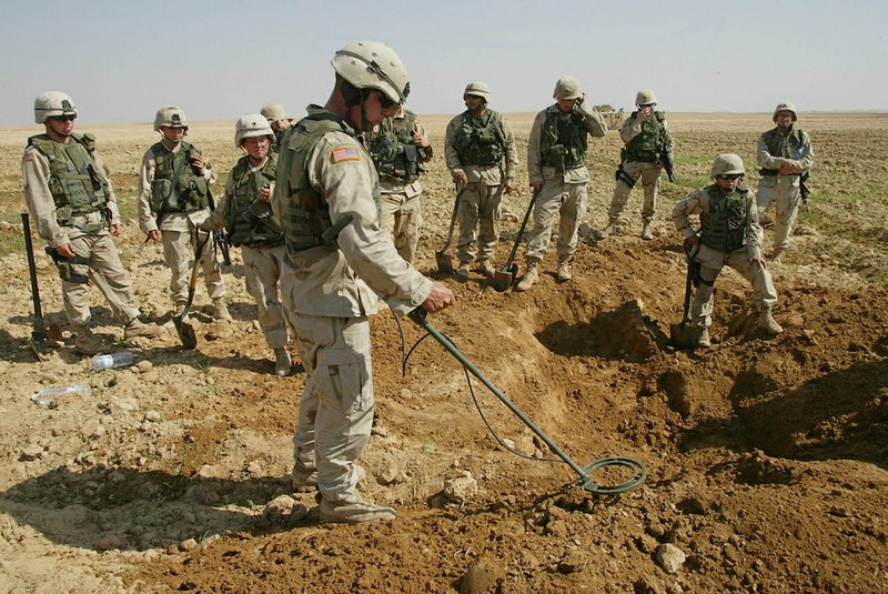 This Oct. 9, 2003, file photo shows soldiers from the U.S. Army's 720th Military Police Battalion watching as a mine sweeper look for weapons in a hole they dug during a raid on a farmland just outside Tikrit, Iraq. 