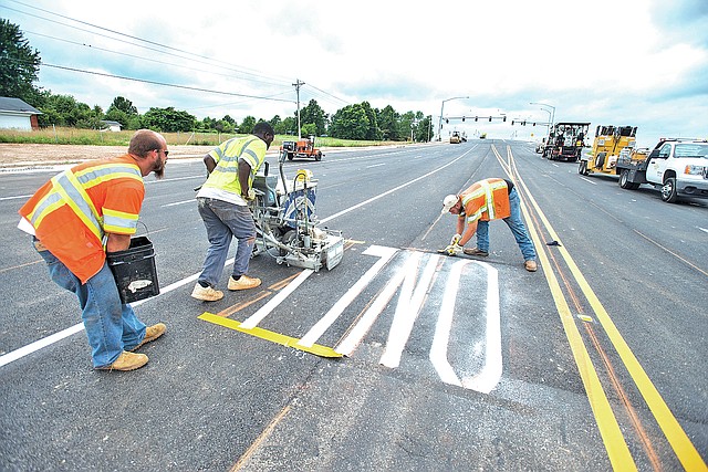 STAFF PHOTO ANTHONY REYES Wheeler, from left, Benson and Kelly finish up striping letters for a turn lane on the Tyson Parkway interchange with Interstate 49 in Springdale.