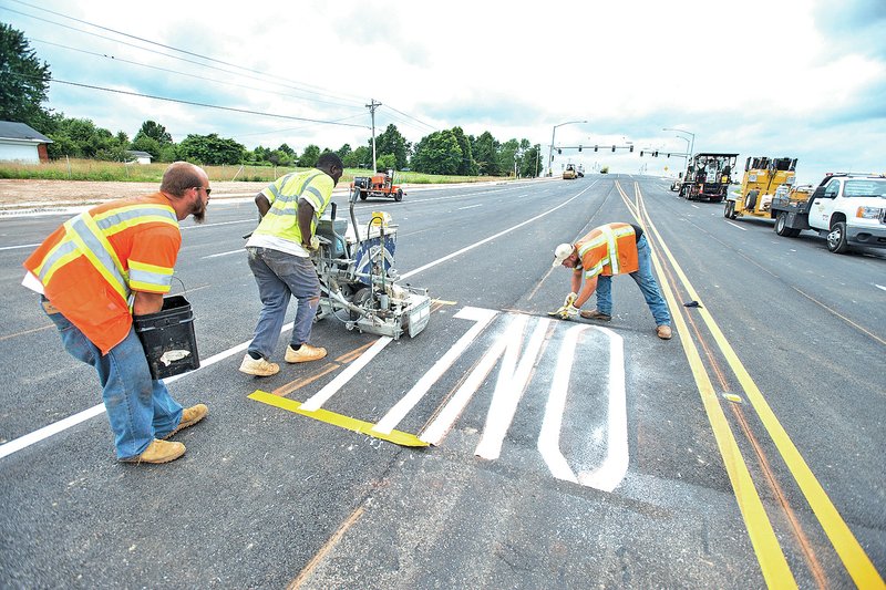 STAFF PHOTO ANTHONY REYES Wheeler, from left, Benson and Kelly finish up striping letters for a turn lane on the Tyson Parkway interchange with Interstate 49 in Springdale.