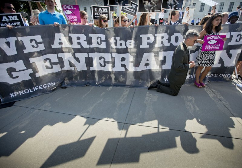 Michael Hichborn kneels and prays as he joins demonstrators while waiting for the Supreme Court's decision on the Hobby Lobby case outside the Supreme Court in Washington on Monday, June 30, 2014. 