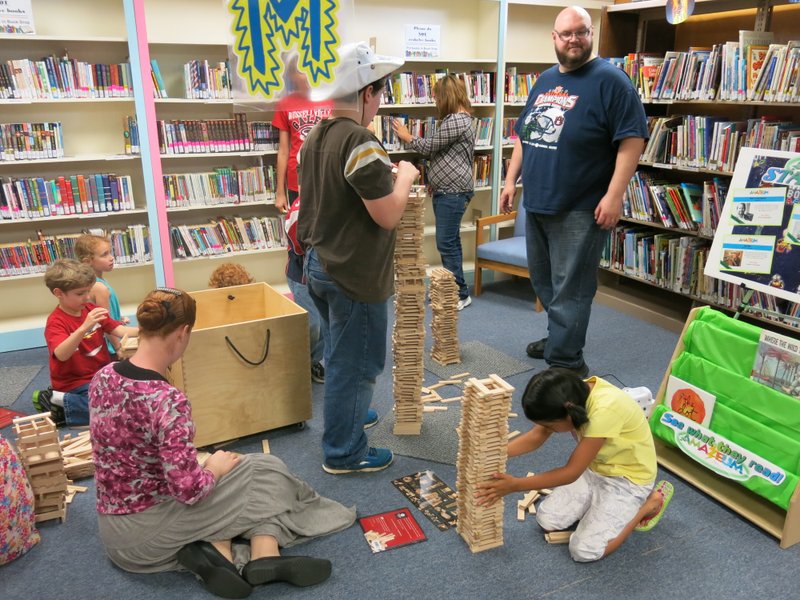 Photo by Susan Holland Several youngsters were busy building structures with Kevlar planks at last Thursday&#8217;s &#8220;Amazeum Science&#8221; summer reading program session at the Gravette Public Library. Jonathon Mills, of Springdale, standing at right, is an Amazeum program volunteer. He supervised the construction of towers, bridges and buildings and measured them as &#8220;knee height,&#8221; &#8220;waist height,&#8221; &#8220;shoulder height&#8221; and &#8220;head height.&#8221; Mills cheered the builders on and encouraged their efforts until the structures toppled to the floor.