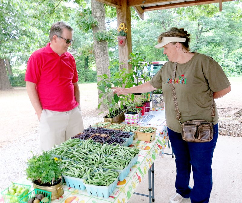 Photo by Susan Holland Evelyn McGraw, right, identifies the variety of a pepper for one of the customers at her booth in the Gravette Farmers Market. Evelyn, who is volunteer co-manager of the market in Old Town Park, has had a booth there for six years and offers a wide variety of popular items, including plants, vegetables, flowers and craft items. The market is open from 8 a.m. to 1 p.m. each Saturday and will be open through November.