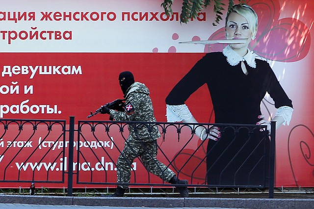 A pro-Russian fighter runs past a huge poster during fighting near a regional police department in downtown Donetsk, eastern Ukraine, Tuesday, July 1, 2014. Ukraine renewed its attacks against armed pro-Russian separatists Tuesday after the president called off a unilateral cease-fire, carrying out air and artillery strikes against rebel positions in eastern Ukraine.