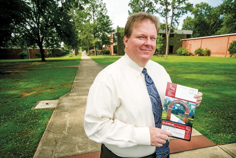 Keith Pinchback, vice chancellor for institutional advancement at Arkansas State University-Beebe, stands in front of the location where the school’s arch used to stand. He holds an ASU publication with a rendering of the proposed new arch.
