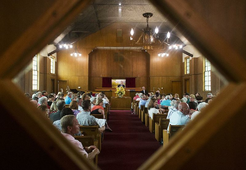 Seen through a window in the sanctuary doors Cary Cox (at the pulpit) invites worshippers to tell stories and share memories of life at Tyler Street Baptist Church during their final service June 29.