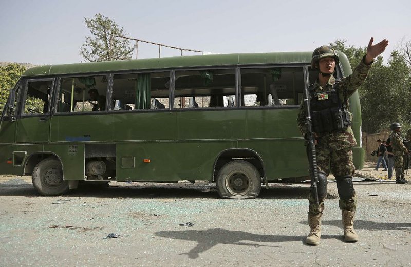 An Afghan soldier tries to get journalists to stop videotaping the scene of a suicide bomb attack on a military bus Wednesday in Kabul that left at least 11 people dead.