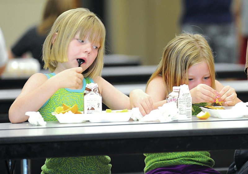 STAFF PHOTO ANDY SHUPE Shaye Hollingsworth, 6, left, eyes twin sister Heaven&#8217;s lunch Tuesday in the cafeteria at Holt Middle School in Fayetteville. The summer lunch program provided by Fayetteville Public Schools, provides 400 free lunches daily for children up to 18 years old.