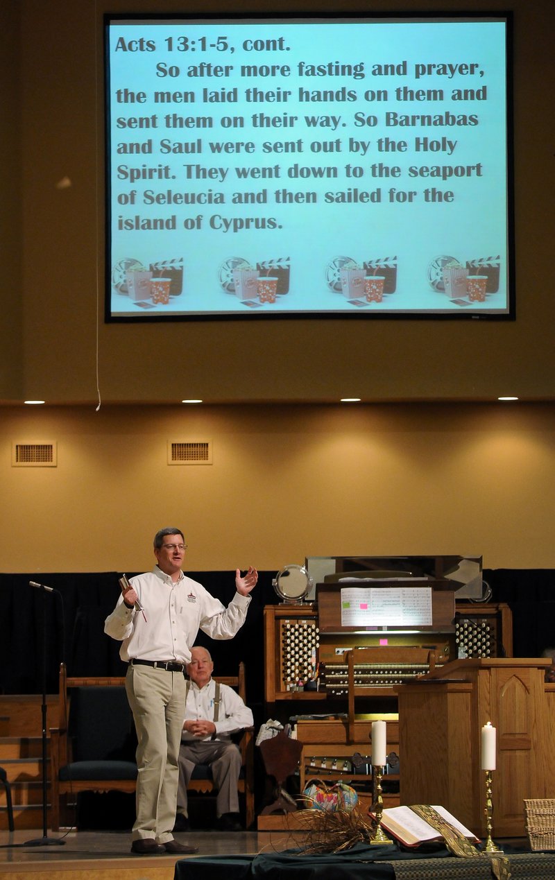 STAFF PHOTO BEN GOFF &#8226; @NWABenGoff The Rev. Carness Vaughan speaks June 29 during a sermon in the Summer at the Movies sermon series at Central United Methodist Church in Rogers. Vaughan interspersed showing clips from the movies &#8220;Up,&#8221; &#8220;The Sandlot&#8221; and &#8220;The Blind Side&#8221; on the screen, top, with his sermon on the theme &#8220;answering the call.&#8221;