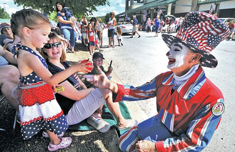 STAFF PHOTO BEN GOFF &#8226; @NWABenGoff Orren &#8216;Bubbles&#8217; Moshinski makes a balloon apple Friday for Stella Witt, 2, of Bentonville during the Fourth of July parade at Sugar Creek Center in Bella Vista.