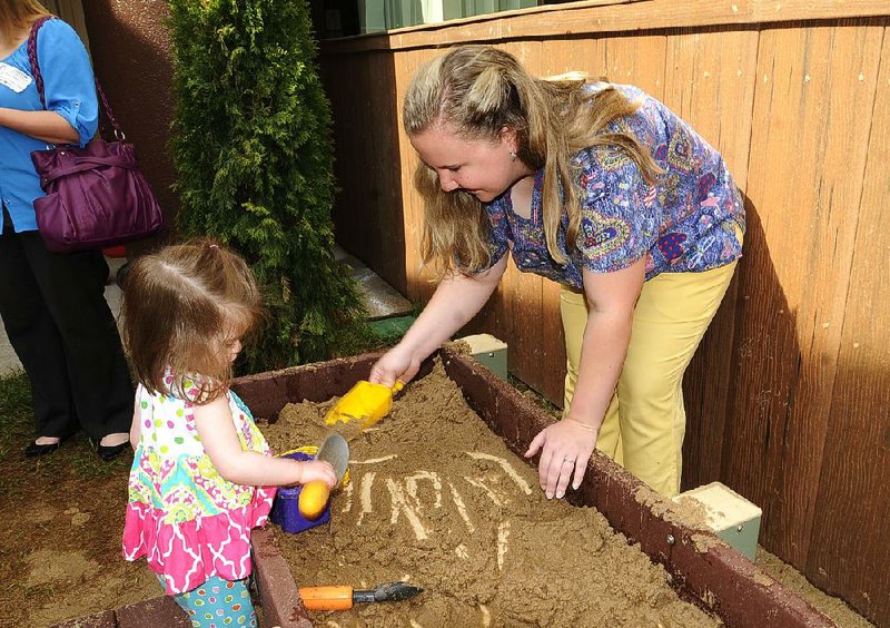 Lyla Tustison, 18 months, and teacher Miranda Bell play in a sandbox June 24 at the new nature playground at the Helen R. Walton Children’s Enrichment Center in Bentonville. The renovated playground for infants and toddlers encourages sensory discovery and development of motor skills through interaction with the environment.