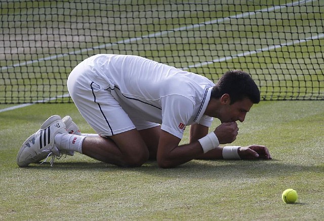 Novak Djokovic of Serbia eats the grass on centre court as he celebrates defeating Roger Federer of Switzerland in the men's singles final at the All England Lawn Tennis Championships in Wimbledon, London, Sunday July 6, 2014. (AP Photo/Pavel Golovkin)