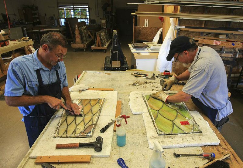 Nathan Cathey (left) and Lynn Fitzgerald remove caulk from panels of stained glass in a workshop in North Little Rock as part of the restoration of the House chambers at the state Capitol.