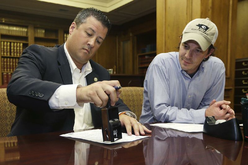 Rob Hammons, director of elections for the Arkansas Secretary of State's office, left, stamps paperwork for  ballot measure petitions as John Whiteside watches at the Arkansas state Capitol in Little Rock, Ark., Monday, July 7, 2014. Whiteside brought boxes of petitions to the office for a ballot measure to increase the state's minimum wage. (AP Photo/Danny Johnston)