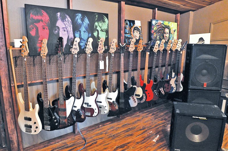 STAFF PHOTO BEN GOFF &#8226; @NWABenGoff Bass guitars hang on display along with paintings, including a portrait of The Beatles by local artist Paula Bonacker, left, in the new Meteor Guitar Gallery.