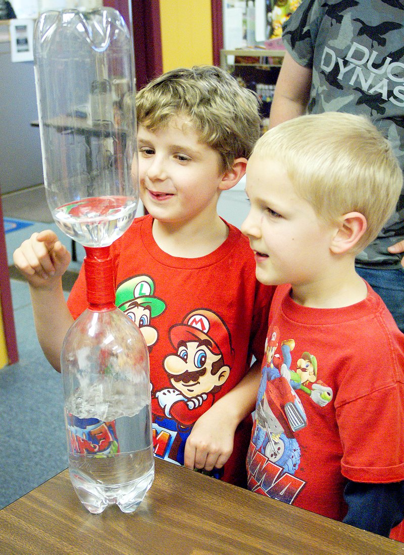 Photo by Randy Moll Matthew and Zach watched the water form a funnel, similar to that formed by the winds of a tornado, as it flowed between the two pop bottles during a children&#8217;s summer reading session at the Gravette Public Library.