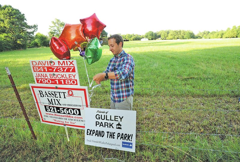 STAFF PHOTO ANDY SHUPE Volunteer Max Mahler attaches balloons to a sign Thursday while giving tours of an 11-acre pasture north of Gulley Park in Fayetteville.