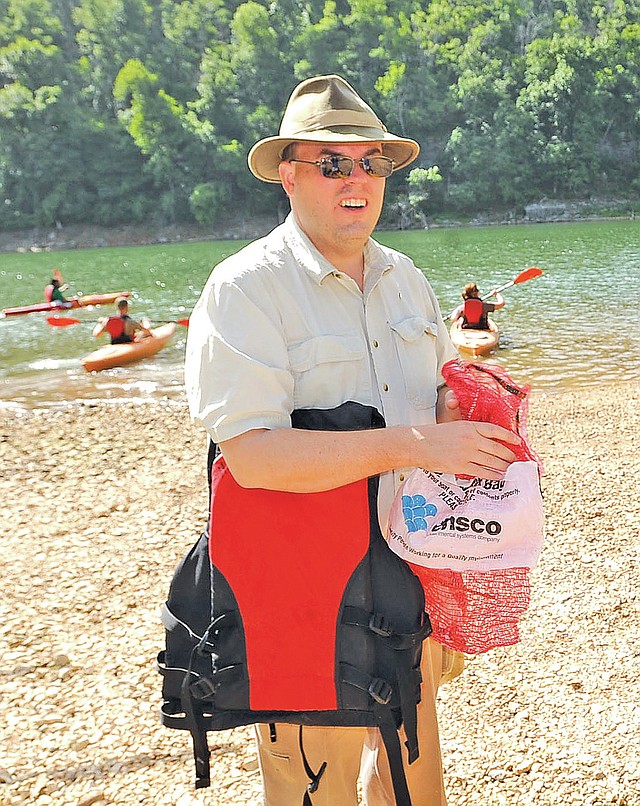 STAFF PHOTO FLIP PUTTHOFF William Armacost of Fayetteville stuffs litter in a sack before heading out with a group in kayaks Saturday.