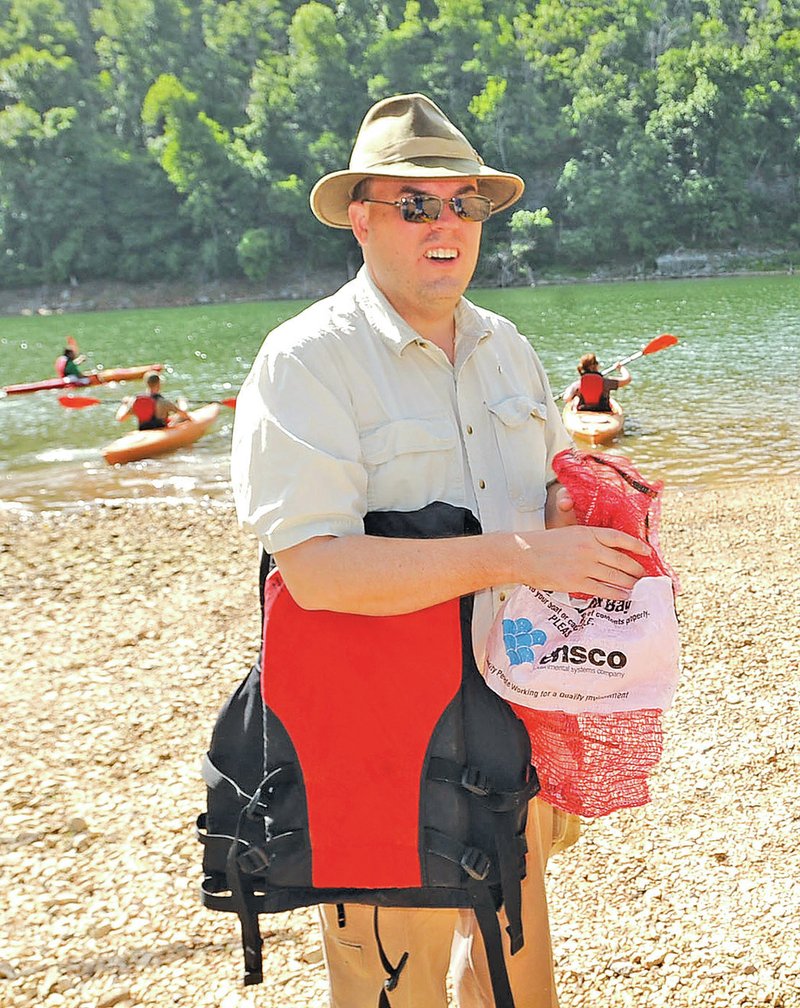 STAFF PHOTO FLIP PUTTHOFF William Armacost of Fayetteville stuffs litter in a sack before heading out with a group in kayaks Saturday.