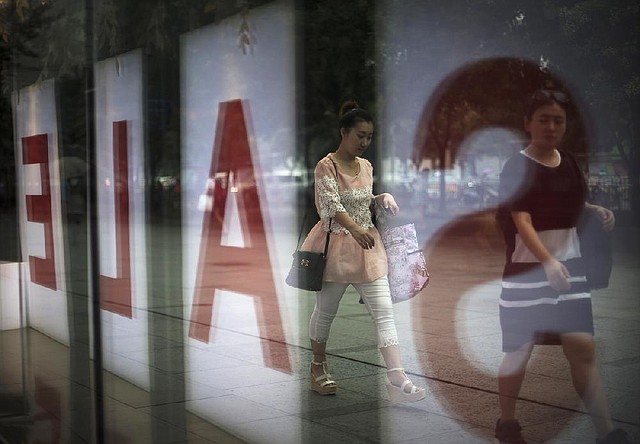 Pedestrians pass a clothing store Wednesday at a shopping mall in Beijing advertising a summer sale. China’s economy grew in the last quarter and more than 7 million new jobs were created.