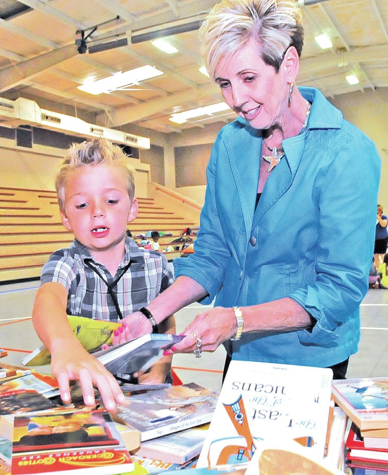 STAFF PHOTO FLIP PUTTHOFF Austin Morrison, 6, gets help selecting a book Wednesday from Frances Rankin with Altrusa of Rogers during the Altrusa literacy fair at the Rogers Activity Center. Friendly Bookstore, which benefits the Rogers Public Library, collects the books through the year and donates them for the literacy fair.