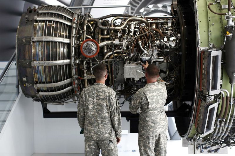 Military personnel look at a GEnx aircraft engine, produced by General Electric Co. (GE), as it stands on display at the company's chalet on the first day of the Farnborough International Airshow in Farnborough, U.K., on Monday, July 14, 2014. The Farnborough International Air Show, which runs July 14-20, is this year's biggest forum for aircraft introductions and sales. Photographer: Simon Dawson/Bloomberg