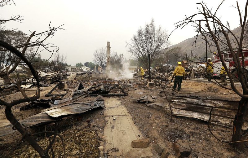 Firefighters work on the still-smoldering remains of a house destroyed the night before in a wildfire, Friday, July 18, 2014, in Pateros, Wash. A fire racing through rural north-central Washington destroyed about 100 homes, leaving behind smoldering rubble, solitary brick chimneys and burned-out automobiles as it blackened hundreds of square miles. Friday's dawn revealed dramatic devastation, with the Okanagan County town of Pateros, home to 650 people, hit especially hard. (AP Photo/Elaine Thompson)