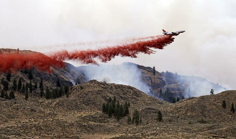 A DC-10 air tanker drops fire retardant over a wildfire Saturday, July 19, 2014, near Carlton, Wash. A wind-driven, lightning-caused wildfire racing through rural north-central Washington destroyed about 100 homes Thursday and Friday, leaving behind solitary brick chimneys and burned-out automobiles as it blackened hundreds of square miles in the scenic Methow Valley northeast of Seattle. (AP Photo/Elaine Thompson)