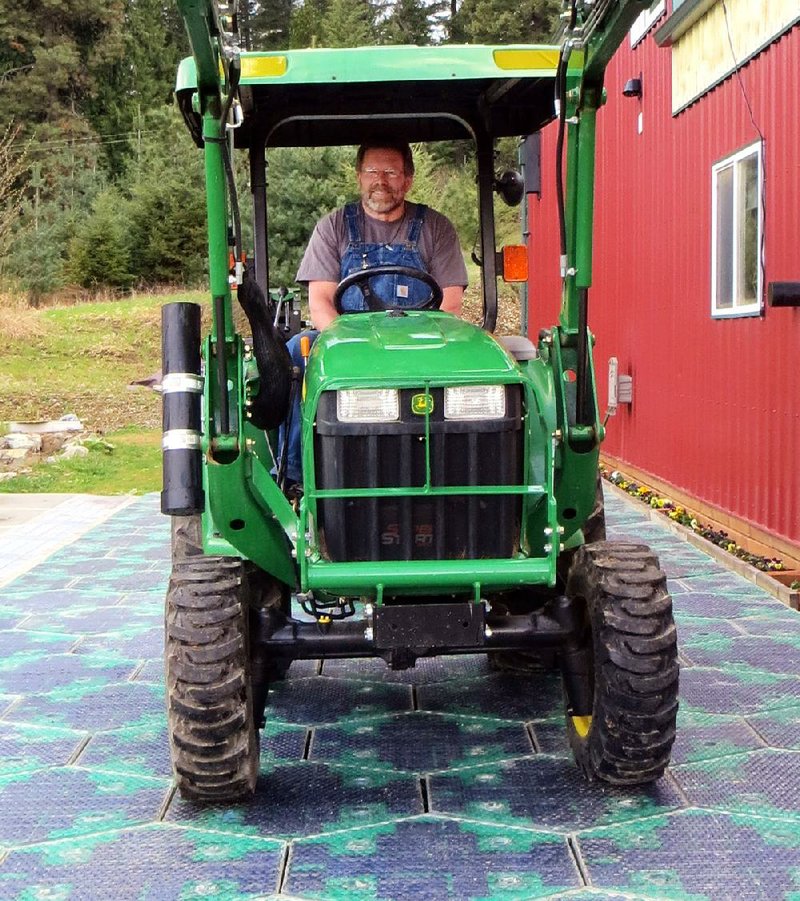 In this May 2014, photo provided by Solar Roadways, Scott Brusaw drives a tractor on a prototype solar-panel parking area at his company's business in Sandpoint, Idaho. Brusaw's idea for solar-powered roads has gone viral and raised more than $1.4 million in crowdsourced funding. Brusaw is proposing to pave driveways, parking lots, bike trails and, eventually, highways with hexagon-shaped solar panels that will produce electricity and could even propel electric cars. (AP Photo/Solar Roadways)