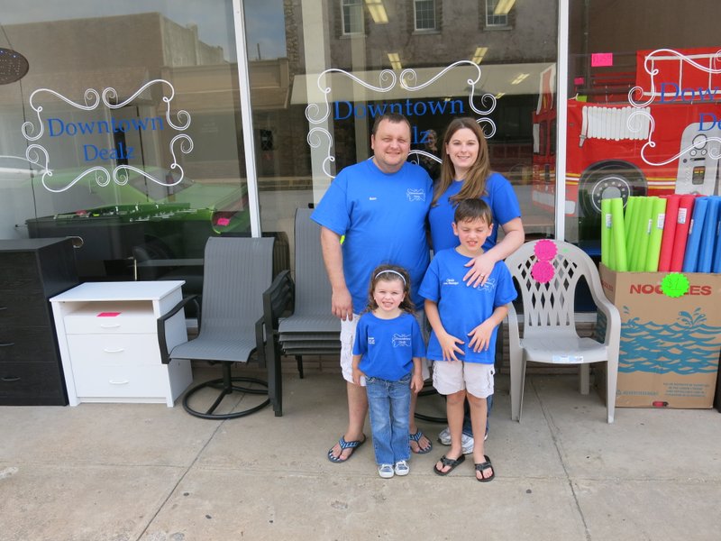 Photo by Susan Holland Downtown Dealz owners Russ and Laura Matney pose with their children, Alyssa, 4, and Chris, 8, in front of the store they recently opened on Gravette Main Street.