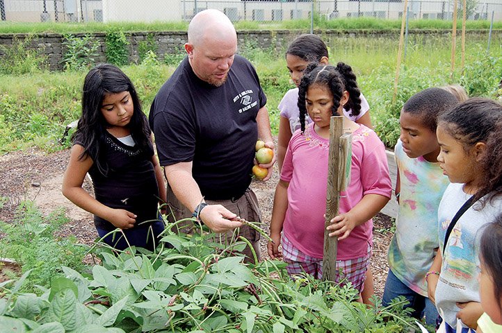 Heath Massey of the Boys & Girls Club of Saline County shows a group of club members that the purple hull peas grown in the club garden are almost ready to harvest. Massey said the children who work in the garden and tend the chickens raised at the club get to select vegetables and eggs to take home. The garden also has flowers and herbs that are sold at the Benton Farmers Market on Thursdays during the summer.