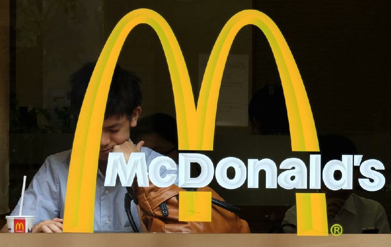 Customers sit behind a logo at a McDonald's restaurant, operated by McDonald's Holdings Co. Japan Ltd., in Tokyo, Japan, on Wednesday, July 23, 2014. Japan suspended food imports from Shanghai Husi Food Co., a unit of Aurora, Illinois-based OSI Group, accused of selling products past their expiration dates as FamilyMart Co. joined McDonaldís Corp. in pulling affected items from its Japanese outlets. Photographer: Yuriko Nakao/Bloomberg