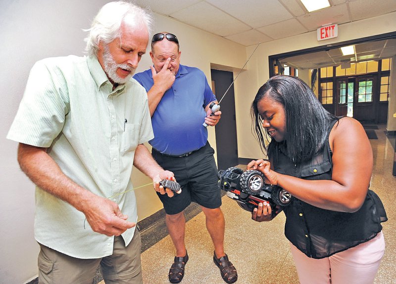 STAFF PHOTO ANDY SHUPE Larry Buell, left, a teacher at West Fork Middle School, helps Karnesia Kelly, right, and John Barton, both teachers at Osceola STEM Academy, to adjust and weigh a radio-controlled car Wednesday before racing it against another during the workshop in Fayetteville.