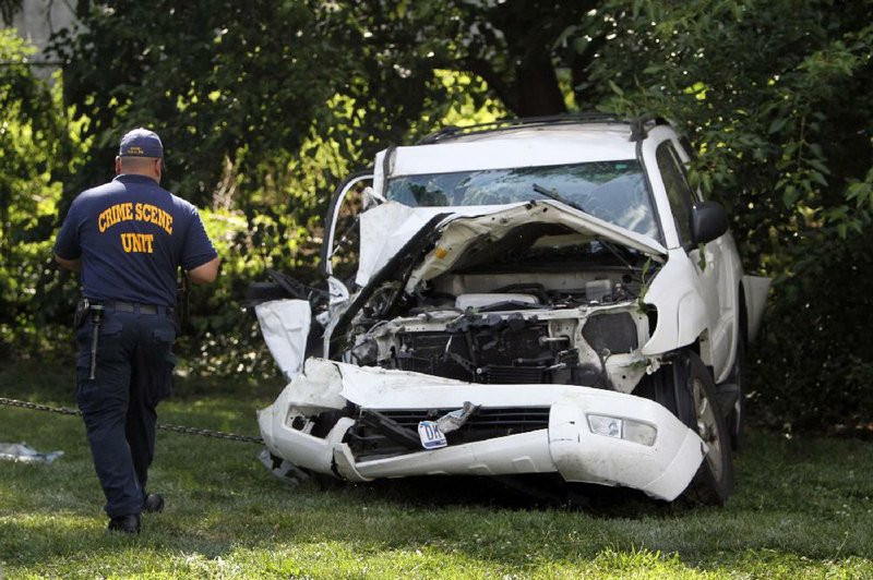 An investigator examines a heavily damaged SUV before it is towed from the scene of a fatal accident in North Philadelphia, Friday July 25, 2014. Two children were killed and three people critically injured when a hijacked car lost control and hit a group of people near a fruit stand, according to police. (AP Photo/ Joseph Kaczmarek)
