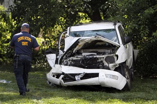 An investigator examines a heavily damaged SUV before it is towed from the scene of a fatal accident in North Philadelphia, Friday July 25, 2014. Two children were killed and three people critically injured when a hijacked car lost control and hit a group of people near a fruit stand, according to police. 