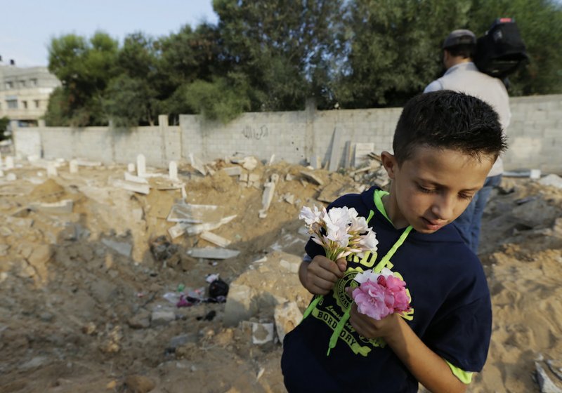 Palestinian Saeb Afana, 12, stands on the edge of a large crater from an Israeli missile strike that destroyed several graves, as he carries flowers at a cemetery in Gaza City, in the northern Gaza Strip, on Monday, July 28, 2014, to visit the grave of a relative, Ayman Afana, 24, who had been killed in an airstrike in the Sheik Radwan neighborhood some 10 days ago. 