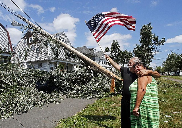 Homeowner Lenny DiBartolomeo hugs his neighbor Jeanie Stornaiuolo while waving a flag in Revere, Mass., Monday, July 28, 2014 after a tornado touched down. Both said they were grateful that they knew of no injuries despite the damage to their homes. (AP Photo/Elise Amendola)