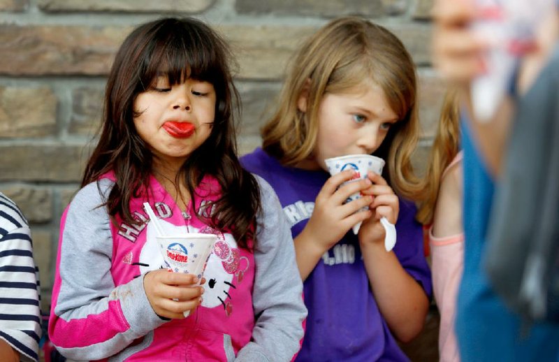 Zuri Aguilar (left) tries to see her tongue as she and Ella Estes enjoy snow cones June 5, the last day of school at Cooper Elementary School in Bella Vista.
