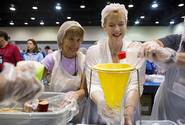 Debbie Wilkinson (left), wife of Georgia state Sen. John Wilkinson, and Amy M. Bailey pack meals while volunteering with the Arkansas Hunger Relief Alliance on Sunday at the Statehouse Convention Center during the Southern Legislative Conference.