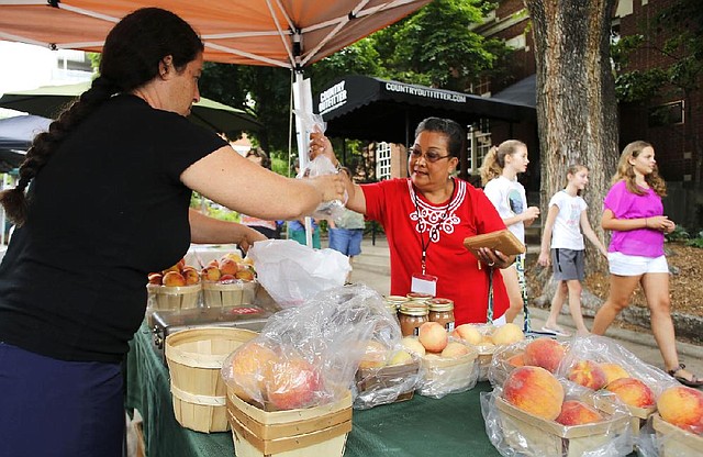 Lydia Astorga (right), a grants and agreements specialist with the Education Division in the U.S. Agriculture Department’s Risk Management Agency, makes a purchase from Alex Munson from A and A Orchard of Green Forest on Thursday at the Fayetteville Farmers’ Market.