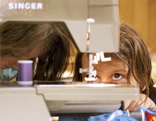 Vivian Norton, 8 (right), watches her sewing project as Belle McKelvey, 8, assists during a three-day sewing clinic for children conducted by Arkansas Extended Learning Center in the Cammack Village Community Center.